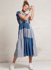 An indigo and denim two-tone, patchwork, midi tiered dress with capped sleeves, pleated detail on the neckline and at the back, elastic waist and slits on the skirt made from yarn dye washed linen