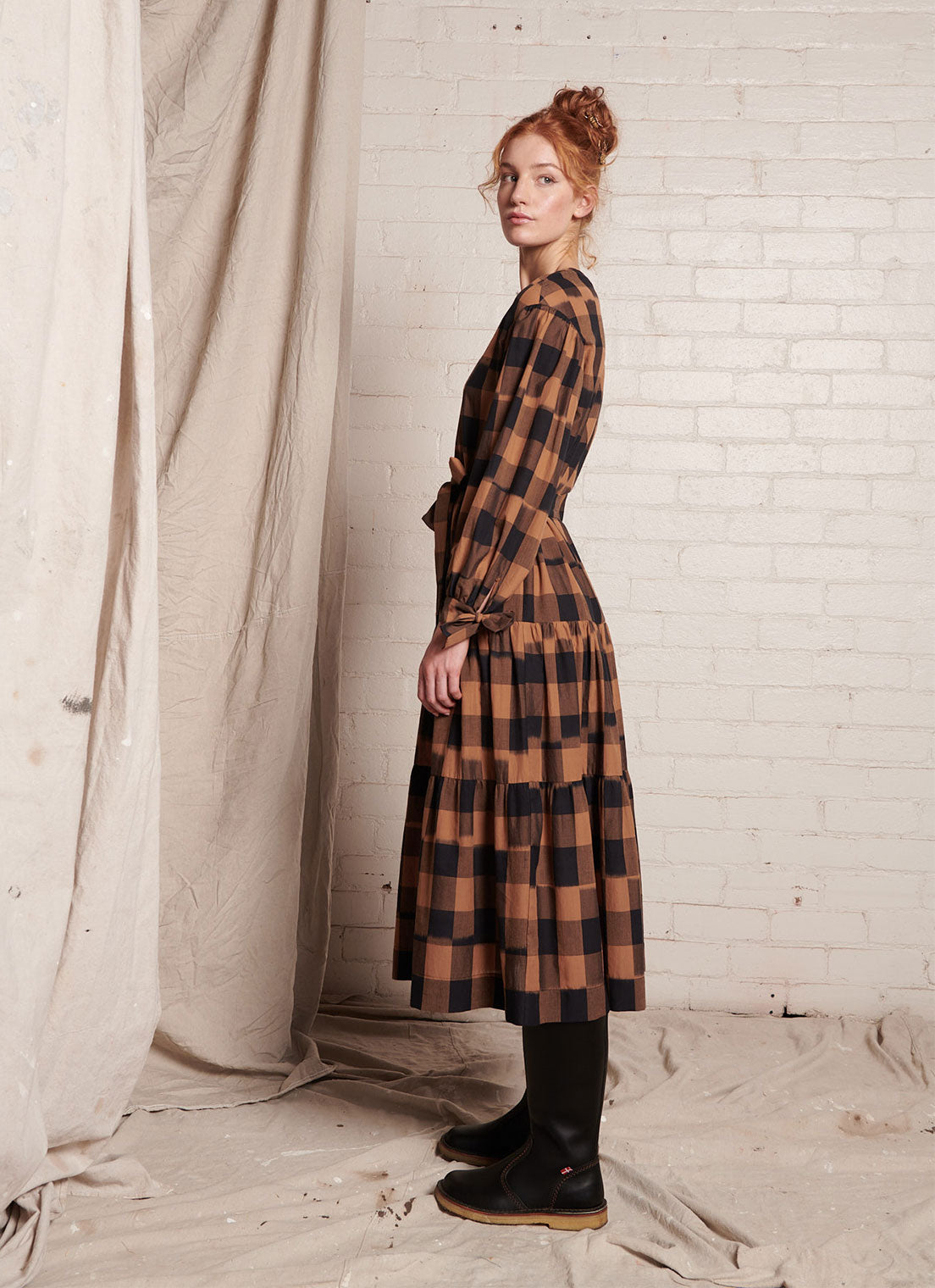 A bronze plaid, midi-length dress with centre front button fastening, round neckline and wrist ties closure made from handwoven ikat cotton