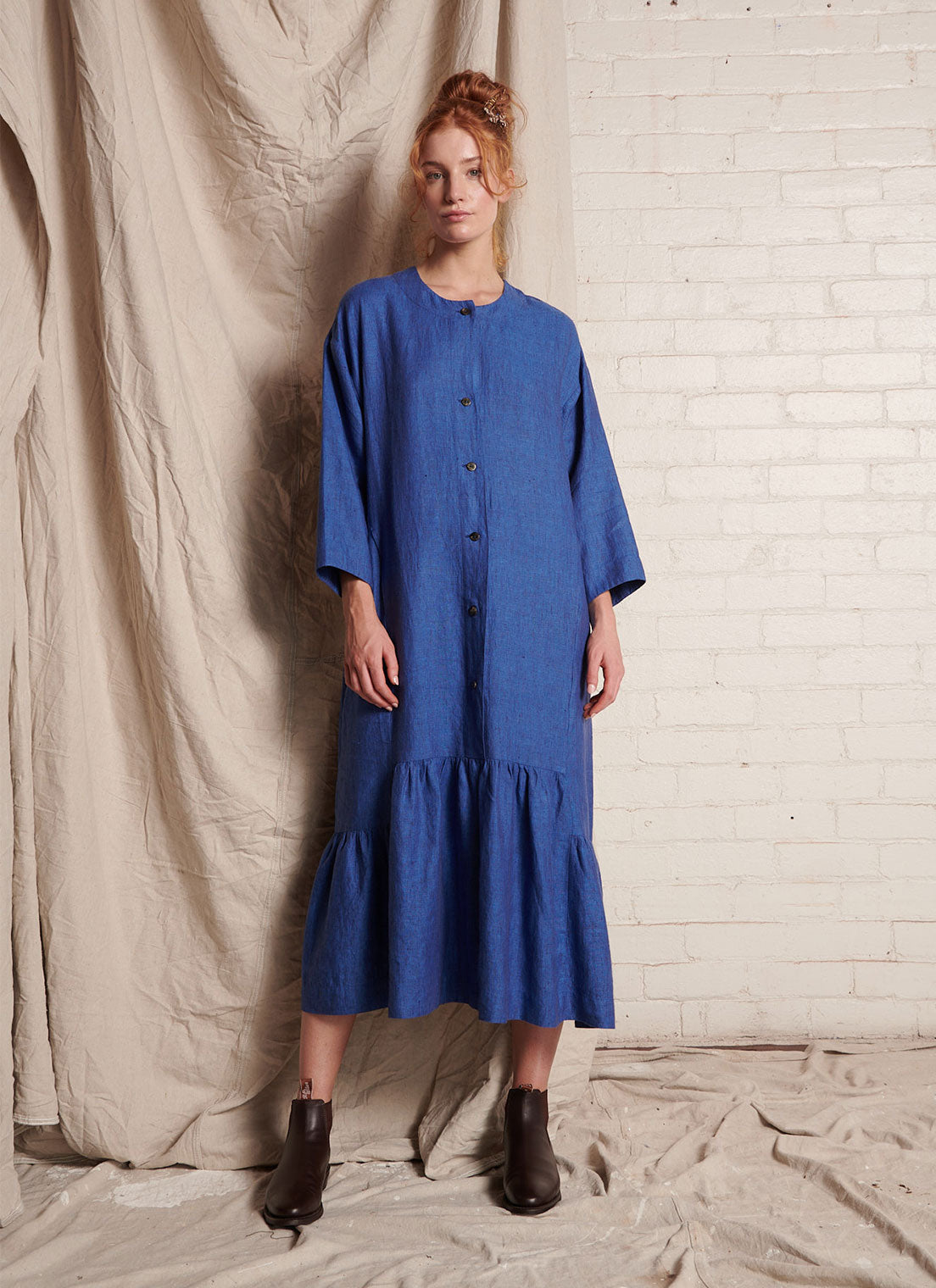 A blue, easy fit, midi-length dress with round neckline, long sleeves, centre front button fastening, flounced hem and embroidered detail at the back made from European pure linen